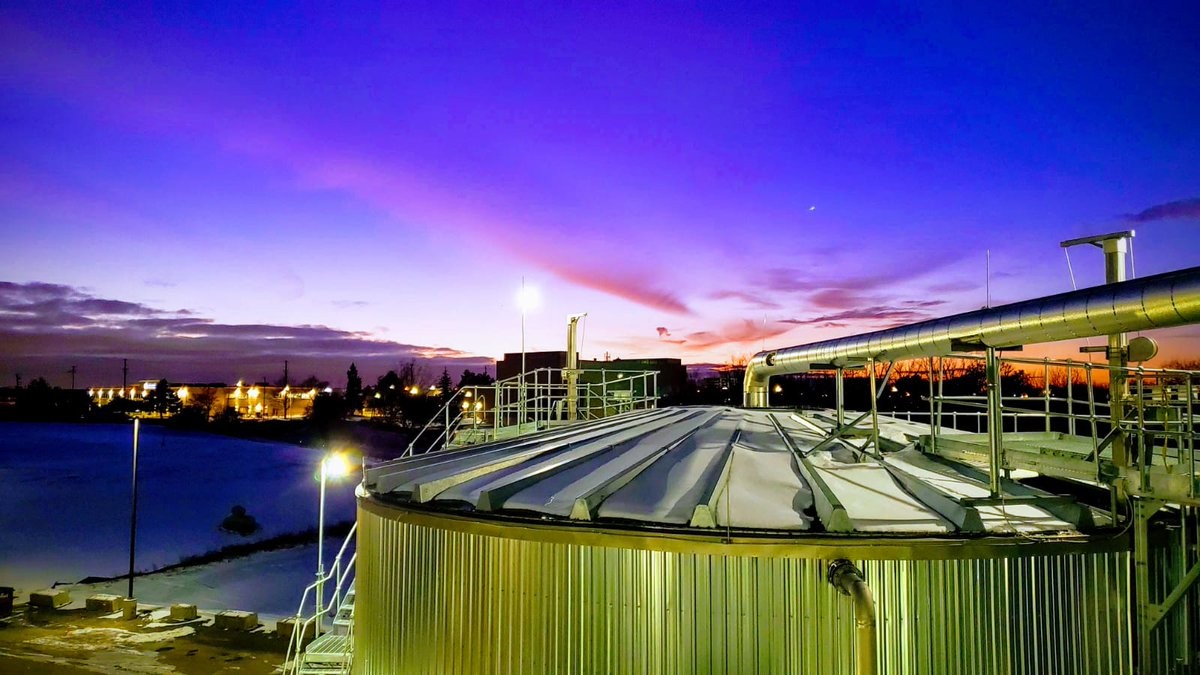 Biogas plant surrounded by green agricultural fields at sunset, representing Anaergia’s renewable energy and biomethane production facilities.